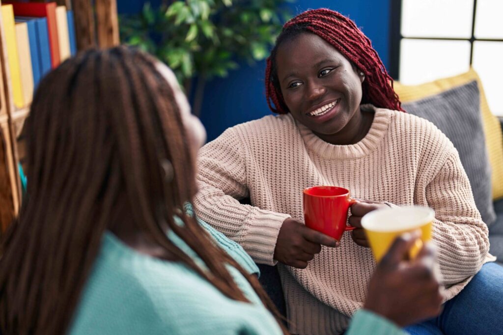 african american women friends drinking coffee sitting sofa home compressed e1703696991410